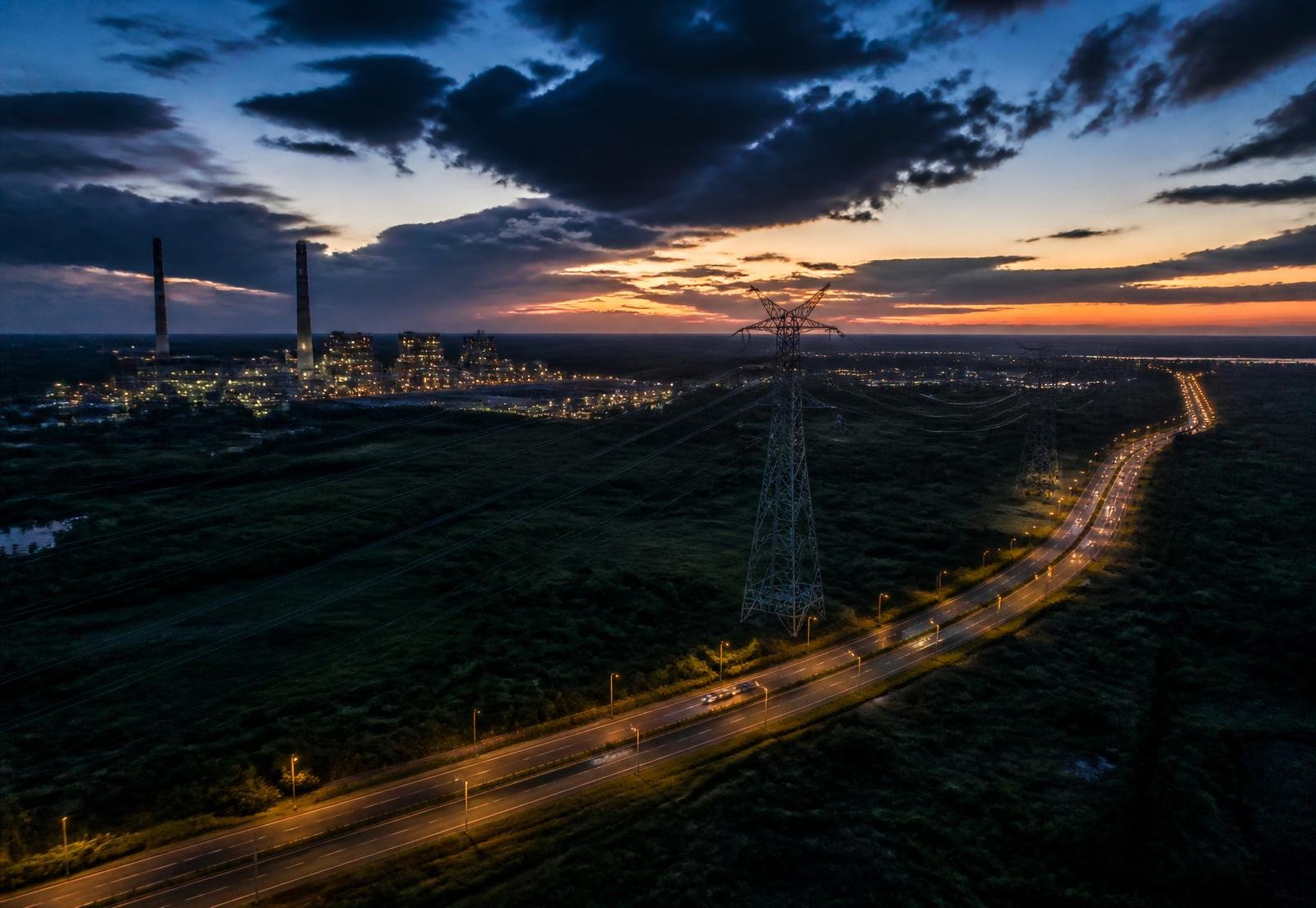 Aerial view of power transmission, industrial plant and highway infrastructure at dusk